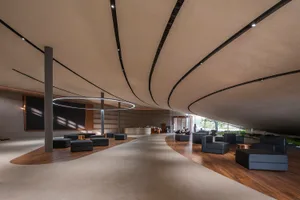 A modern lobby space with curved concrete walls and floors, featuring circular lighting fixtures and contemporary seating arr