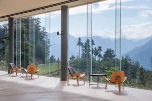 Modern minimalist living room featuring a white floor, large glass windows with a scenic mountain view, and three wooden armc