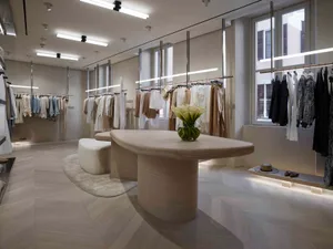 Modern retail store with clothing racks, a wooden central table, and a glass vase with flowers.