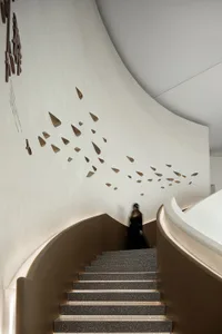 Modern interior featuring a staircase with concrete steps, white textured walls, and abstract artwork resembling dreaming fig
