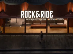 A modern, industrial retail storefront with a large metal sign displaying the name 'Rock & Ride'.