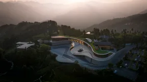 A modern, curving concrete building with a green roof set against a mountainous landscape.