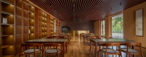 A spacious restaurant interior with wooden furniture and walls, a wooden slatted ceiling, and large windows.