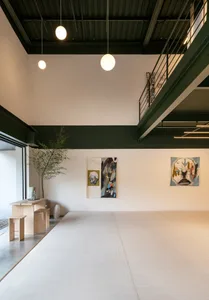 A modern living room with concrete flooring, minimalist furniture, and abstract art on the walls.