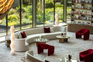 A modern and luxurious hotel lobby with plush seating, marble tables, and a lush green exterior.
