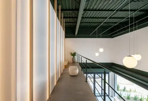 A modern industrial office space featuring concrete flooring and walls, with minimalistic furniture and hanging spherical lig