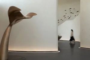 A minimalist interior space featuring concrete elements, with a blurred figure walking through the space.