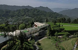 An aerial view of a modern tea room nestled in verdant mountains, showcasing greenery, concrete, and glass materials.
