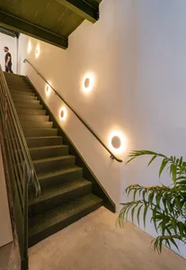 A minimalist staircase with metal steps and a metal railing against a white wall with round lights.