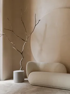 Minimalist interior design featuring a beige sofa with a circular wall feature and a natural branch plant.