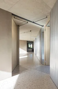 Modern minimalist office interior featuring concrete walls and floors, with natural light entering through large windows.