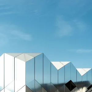 Modern building facade covered in reflective, mirrored glass panels against a clear blue sky.