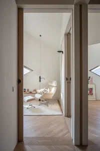 A modern minimalist living room with a wood floor, white walls, and a single white chair with a matching ottoman.