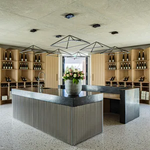 A modern wine-tasting room featuring concrete countertops, wooden shelving, and geometric lighting. Floral arrangement on the
