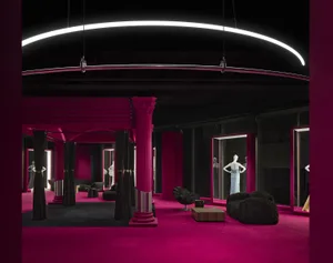 A retail storefront with a vibrant fuchsia color scheme, featuring a high ceiling with a curved LED light fixture and columns