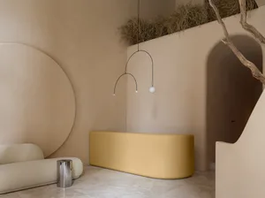 A minimalist interior space featuring a concrete bench and arches, with a metal sculpture hanging overhead and dry grass on t