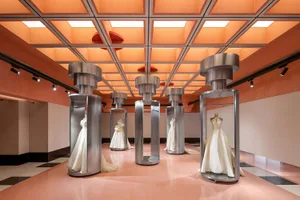 A modern fashion exhibition featuring metal and glass displays with mannequins wearing elegant dresses on wheels with silver,