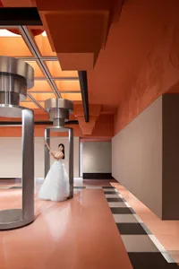 Fashion shoot featuring a woman in a white dress standing in a modern, industrial space with metallic pillars and a geometric