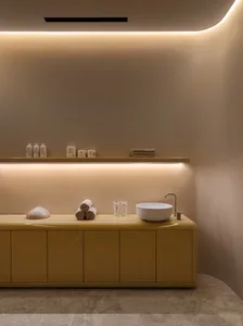 A modern minimalist bathroom with a yellow cabinet, white sink, and beige marble floor.