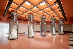 Modern exhibit space featuring glass and metal displays and white dresses.