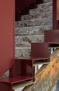 Industrial-style staircase with red metal steps and a weathered, rusted metal wall.
