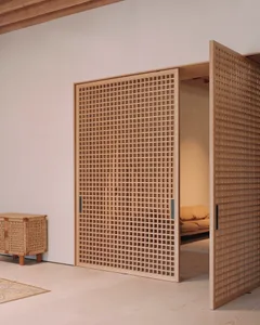 A wooden lattice door with a grid pattern stands open, leading to a room with a futon.