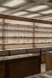 A minimalist optical retail store with wooden shelves and glass showcases displaying eyeglasses and sunglasses.