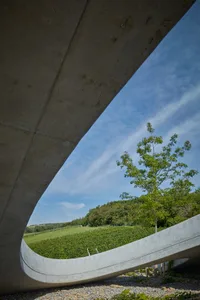 A modern architectural space featuring concrete structures and greenery under a clear blue sky.