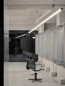 Industrial office space with minimalist concrete desk and chair, glass partitioning, and industrial lighting.