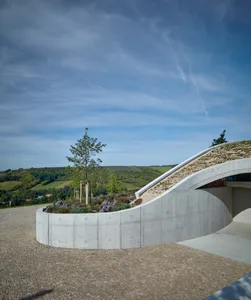 Contemporary landscape design featuring a curving, concrete structure with a green roof and natural surroundings.