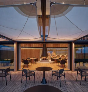 Modern restaurant interior with a central fire pit and wooden tables and chairs.