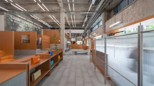 A modern retail storefront with orange metal structures, concrete floors, potted plants, and a minimalist design.