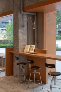 Modern cafe with seating made of concrete, featuring stools and a table with an open book and laptop.