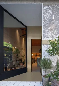 A modern retail storefront with a concrete facade and large glass windows displaying indoor plants and furniture.