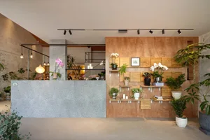 An indoor space featuring a concrete reception counter, wooden walls adorned with plants, and ambient lighting.