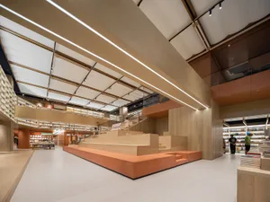 A modern bookstore with a wooden interior featuring numerous bookshelves, steps, and overhead lighting.