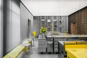Modern minimalist restaurant kitchen featuring metal counters, wooden panels, and yellow accents.