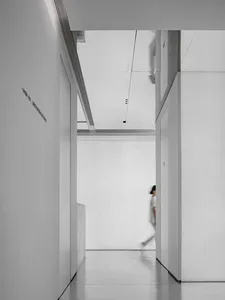 A minimalist white interior featuring a corridor with white walls and floor, leading to a white-walled room.