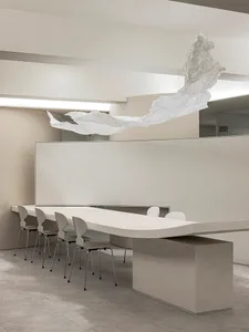 A modern conference room with a minimalist design, featuring a textured concrete table, white chairs, and a floating white pa