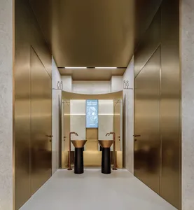 A modern, minimalist hospitality interior featuring metallic brass and textured concrete elements.