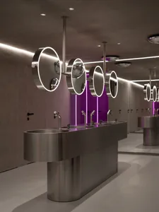 Modern public restroom with metal sinks and glass stalls