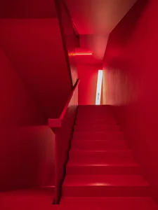 A modern minimalist staircase with red walls and metallic railings.