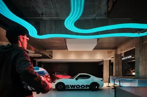 A modern showroom with a white car featuring 'SWOOP' and bright neon lights.