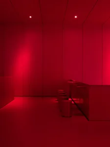 A minimalist interior space with red walls, metallic stools, and a sleek, modern design.