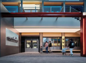A modern industrial storefront with a glass and metal facade, concrete ground level, and concrete stairs leading to a glass s