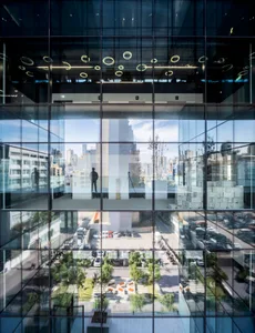 A modern office building with a glass facade viewed from the street level, reflecting the cityscape.