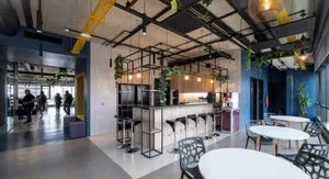A modern, industrial-style office space with concrete floors, metal piping, and a small kitchen area.