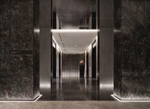 A modern corridor with dark marble walls, illuminated by subtle lighting, leading to a lobby area.