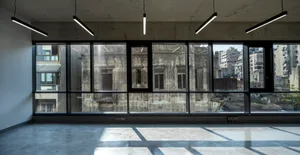 A spacious, empty interior space featuring large glass windows reflecting an urban cityscape.
