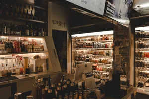 Modern bar with a metallic and glass bar counter on one side and a well-stocked glass shelf on the other, featuring bottles o